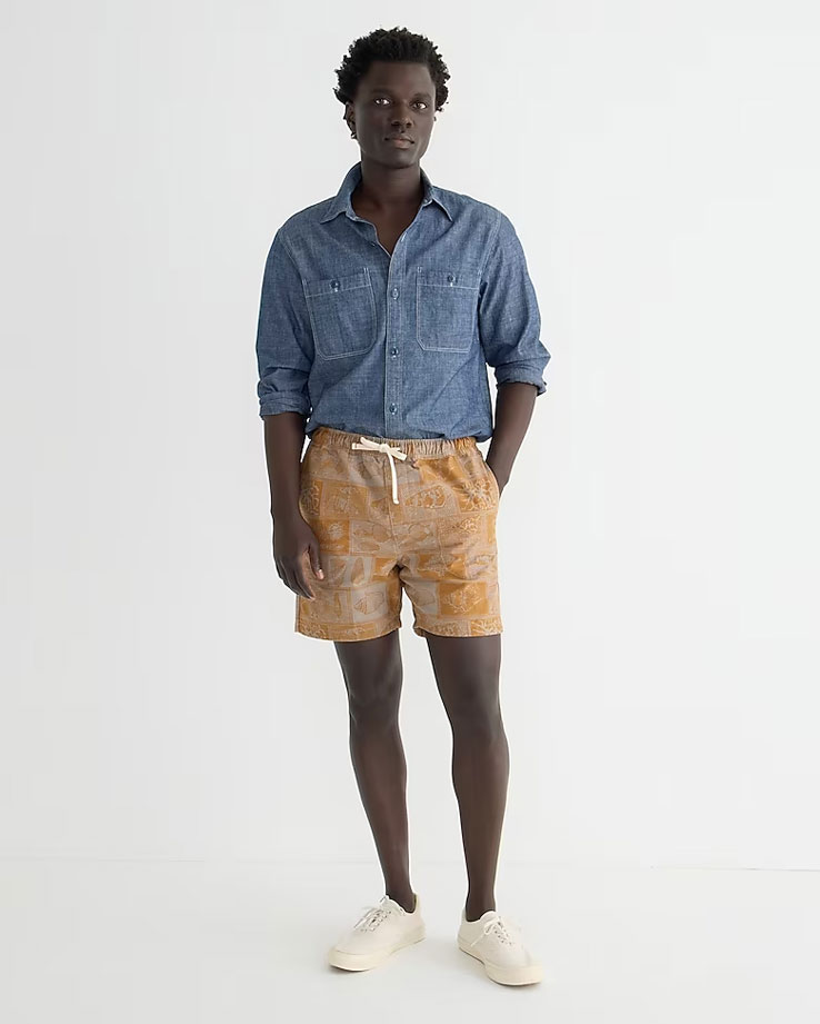 Male model wearing chambray shirt with beach shorts and canvas shoes for a casual summer look.